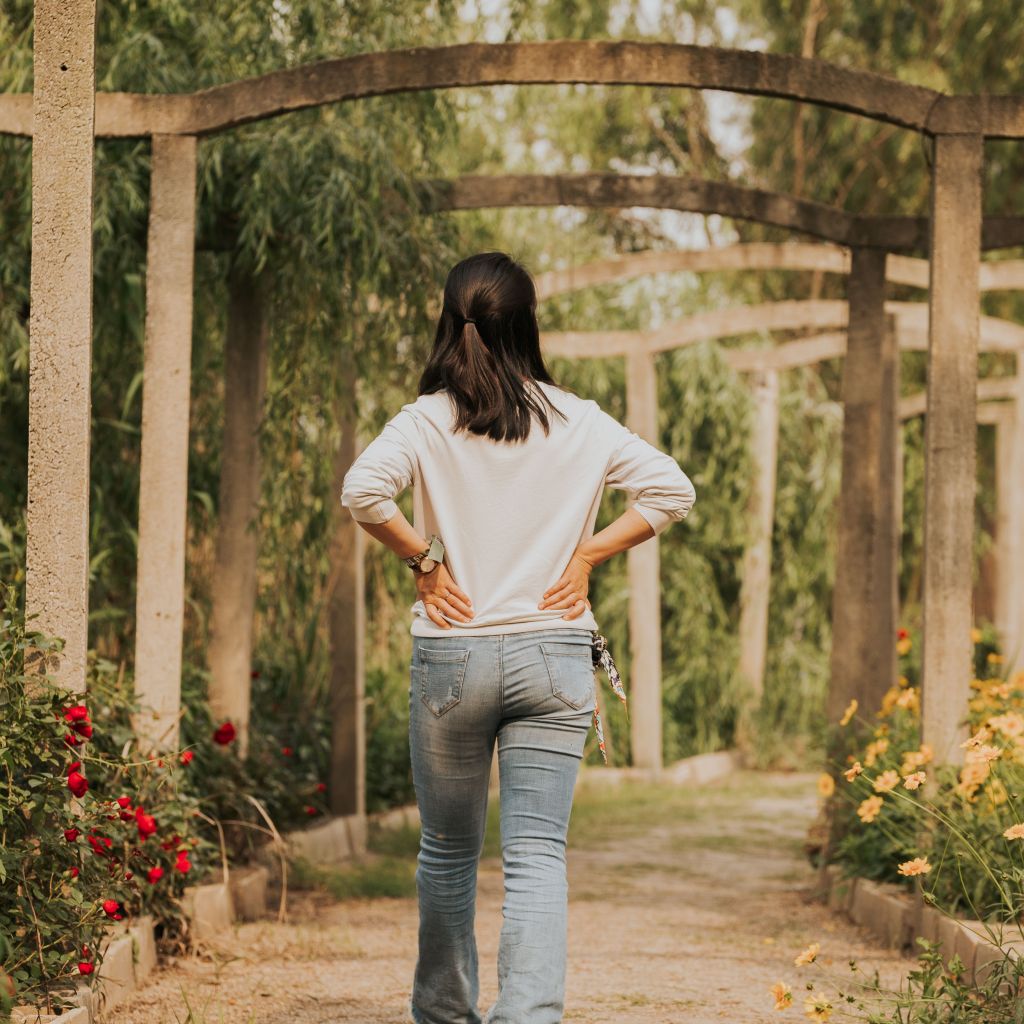 A woman explores a lush garden trail lined with flowers and greenery in spring.